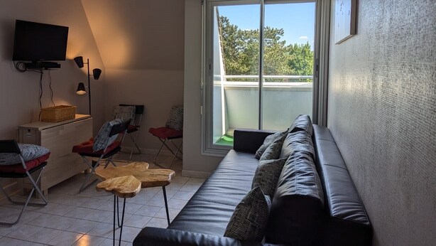 A modern living room with a sofa, chairs, a TV, and a large window offering a view of trees. - New cocoon between sea and countryside 4Pers Private parking (Villers-sur-Mer)