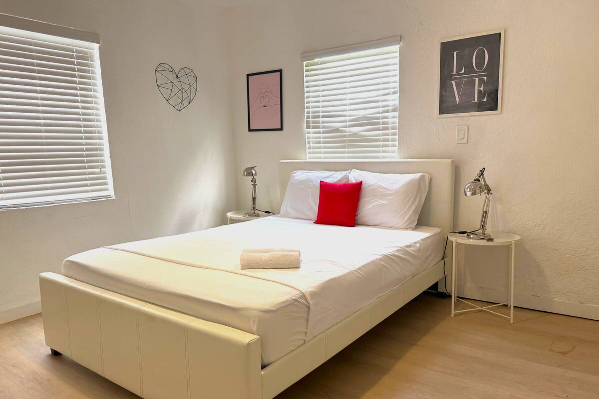 Een keurig opgemaakt slaapkamer met een bed, nachtkastjes en een muur met decoratieve objecten.