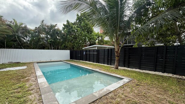 Piscina rectangular con borde de azulejos, rodeada de césped y una cerca negra.