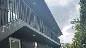 Un edificio moderno con fachada oscura, una escalera que lleva a un balcón y un camino pavimentado.
