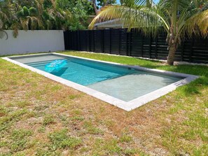 A rectangular swimming pool with clear blue water, surrounded by a grassy area and a black fence. - Wynwood Bungalows By Renzzi (Miami)