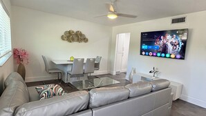 A modern living room with a grey sectional sofa, a glass coffee table, and a flat-screen TV mounted on the wall. - Stylish 1-bed apartment, in East Delray Beach, pets, parking, free laundry (Delray Beach)