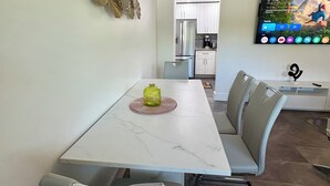 A modern dining area with a white marble table, grey upholstered chairs, and a decorative wall piece. - Stylish 1-bed apartment, in East Delray Beach, pets, parking, free laundry (Delray Beach)