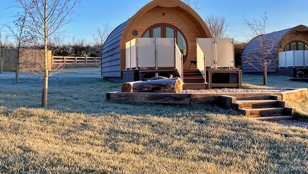 A modern, wooden cabin with a circular window and a wooden deck. - Glamping Pods in Yorkshire Near Coastline (York)