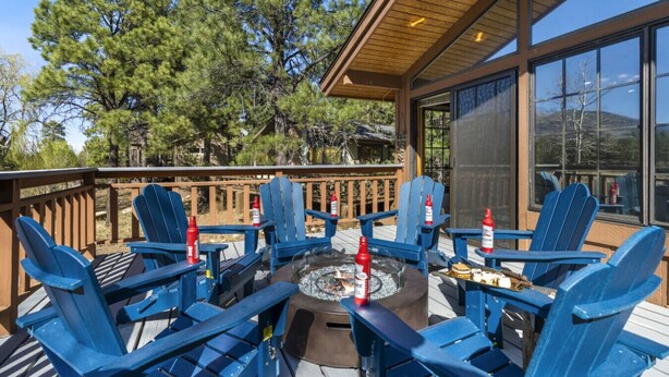 A deck with blue Adirondack chairs, a fire pit, and a glass enclosure.