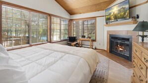 A bedroom with a large bed, a fireplace, a ceiling fan, and large windows with blinds.