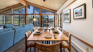 A spacious room with a large dining table, blue sofa, and large windows offering views of the outdoors.