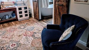 Um quarto com uma poltrona azul escura, um tapete estampado, uma cozinha com fogão e uma janela com cortinas.