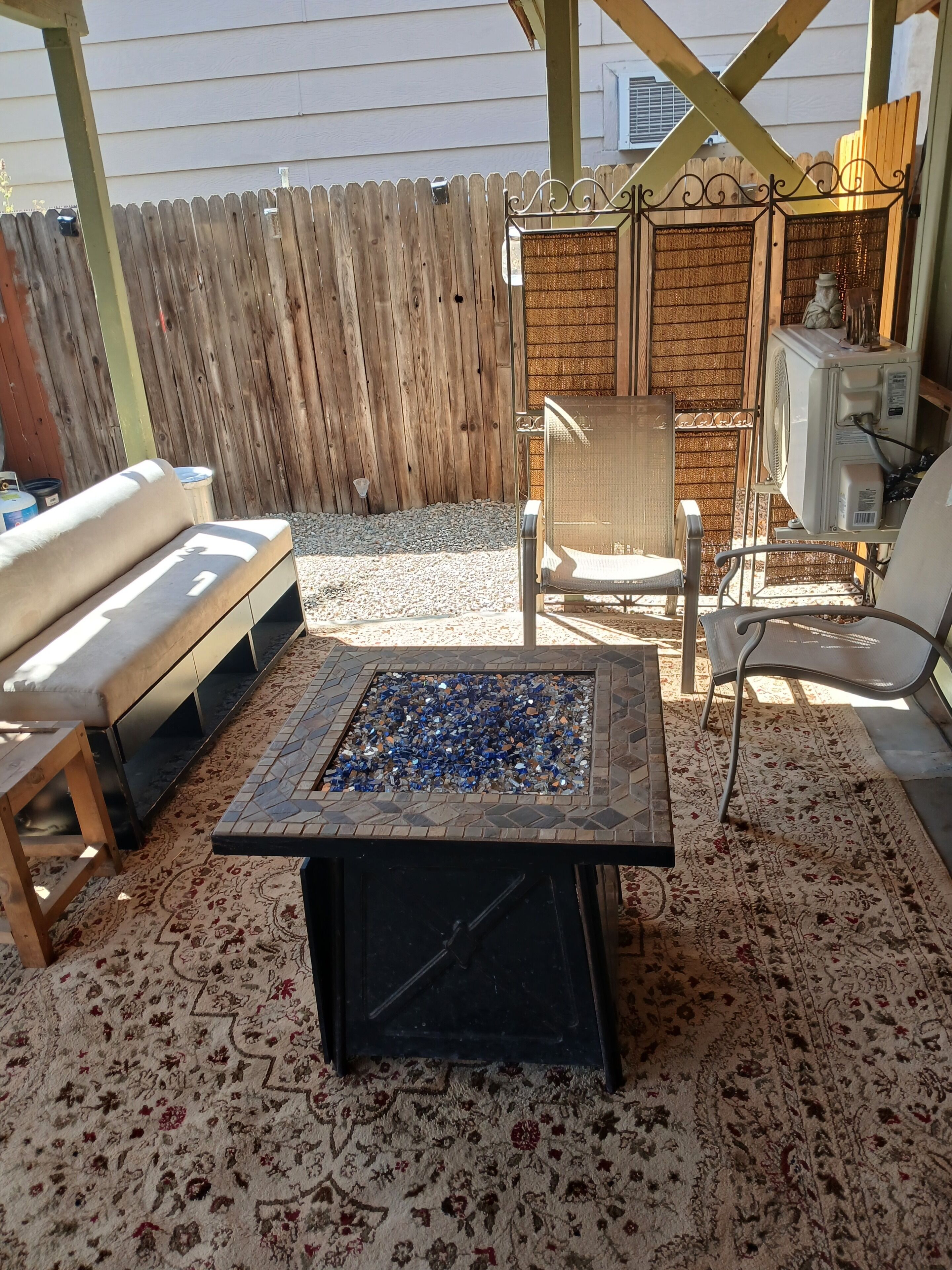 Eine Terrasse mit Feuerstelle, Gartenmöbeln und einem dekorativen Zaun.