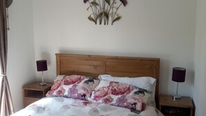 A bedroom with a wooden headboard, floral bedding, two bedside tables with lamps, and a wall-mounted decoration. - Cosy holiday chalet (Cearnarfo)