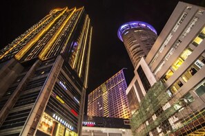 A nighttime view of a cityscape with tall buildings, including a distinctive curved building with illuminated signage. - Qiyue Shangpin Cinema Hotel Apartment (Guanyinqiao Branch) (Chongqing)