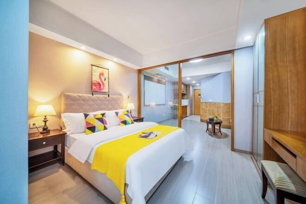 Une chambre d’hôtel moderne, dotée d’un grand lit, de tables de chevet, d’un miroir et donnant sur le couloir.