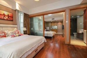 A hotel room with a bed, a desk, a chair, a bathroom, and a glass door leading to another room.