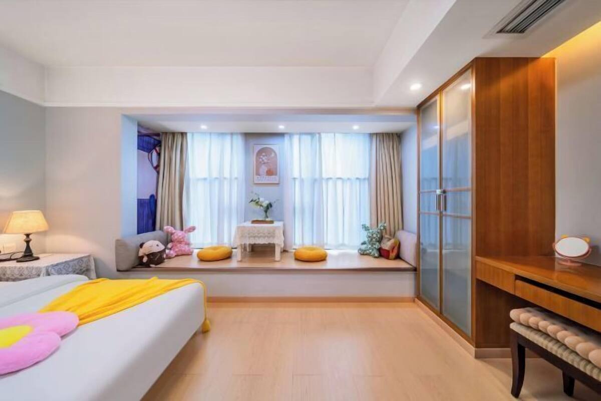 Une chambre à coucher comprenant un lit, une table de chevet, une lampe, une fenêtre avec des rideaux et une armoire en bois.