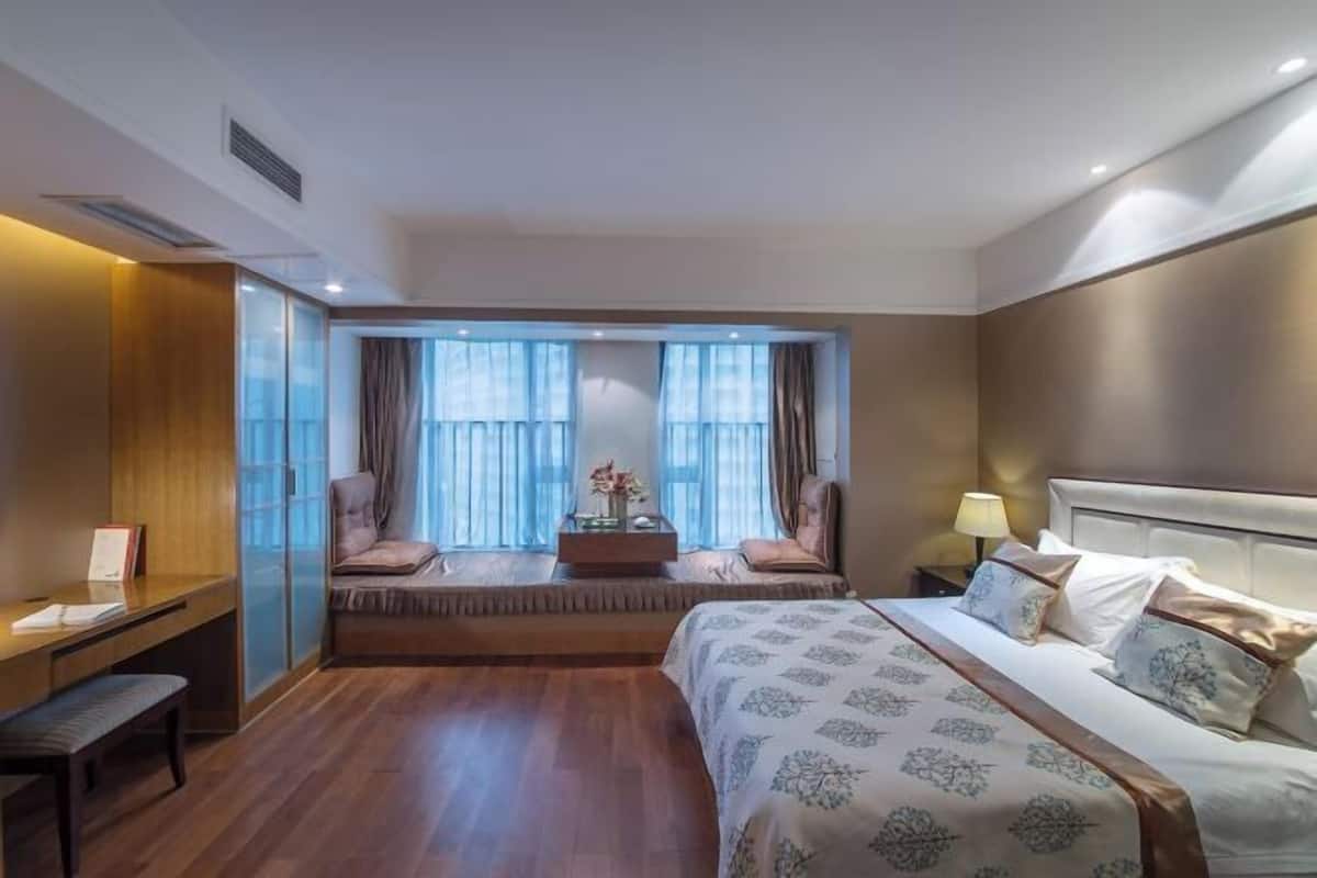 Une chambre d’hôtel avec un grand lit, un bureau, un coin salon avec vue et une fenêtre avec des rideaux.