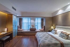 A hotel room with a large bed, a desk, a seating area with a view, and a window with curtains.