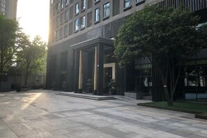 A modern building with a covered entrance, a paved courtyard, and a tree. - Qiyue Shangpin Cinema Hotel Apartment (Guanyinqiao Branch) (Chongqing)