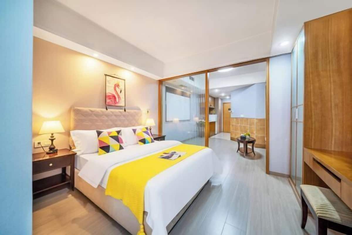 Une chambre d’hôtel moderne dotée d’un grand lit, d’une table de chevet avec une lampe, d’une armoire en bois et d’une cloison en verre donnant sur la salle de bain.