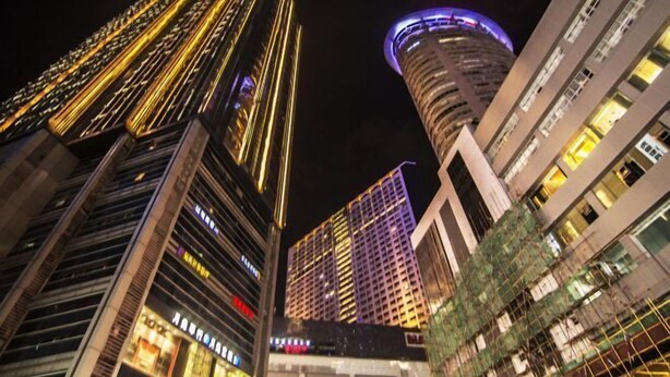 A nighttime cityscape with tall buildings, including a prominent curved skyscraper with a blue-lit top. - Qiyue Shangpin Cinema Hotel Apartment (Guanyinqiao Branch) (Chongqing)