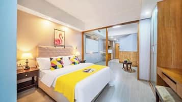 Una habitación de hotel moderna con una cama grande, una mesita de noche con lámpara, un armario de madera y un separador de vidrio que da acceso a un baño.
