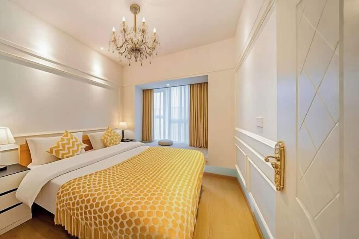 Une chambre d’hôtel avec un grand lit, un lustre, une fenêtre avec des rideaux et une porte dotée d’une poignée.