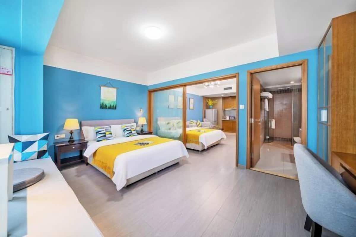 Une chambre d’hôtel avec deux lits, un bureau, une chaise et une salle de bain visible à travers une porte en verre.
