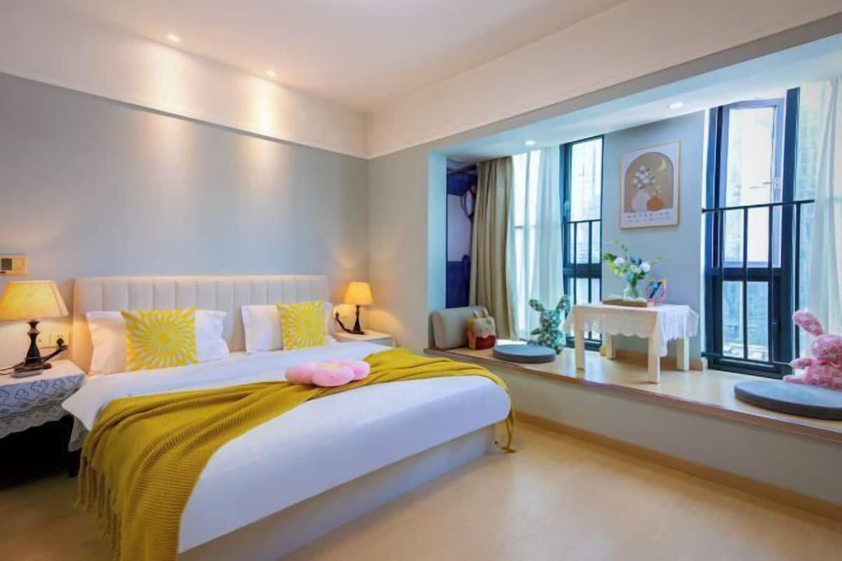 Une chambre d’hôtel avec un lit, des lampes de chevet, une fenêtre avec des rideaux, une petite table avec un vase et un objet décoratif posé sur le rebord de la fenêtre.