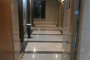 A hallway with a trash bin, a door with a handle, and a wall-mounted light switch. - Qiyue Shangpin Cinema Hotel Apartment (Guanyinqiao Branch) (Chongqing)