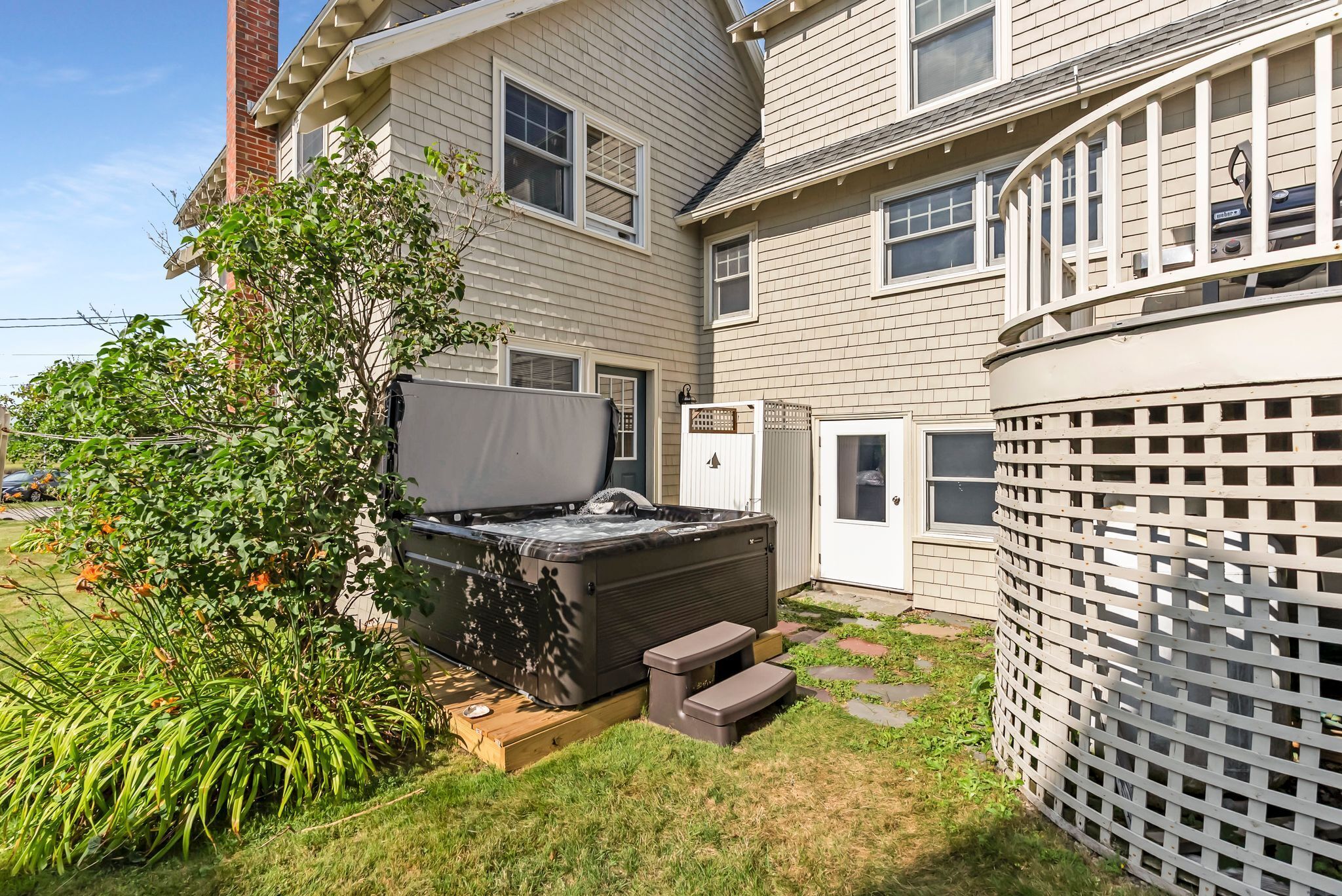 A residential backyard with a hot tub, a wooden deck, and a white fence.
