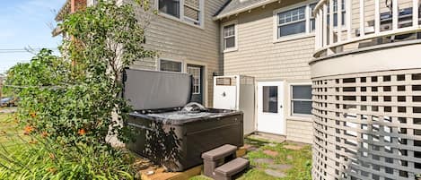 A residential backyard with a hot tub, a wooden deck, and a white fence.