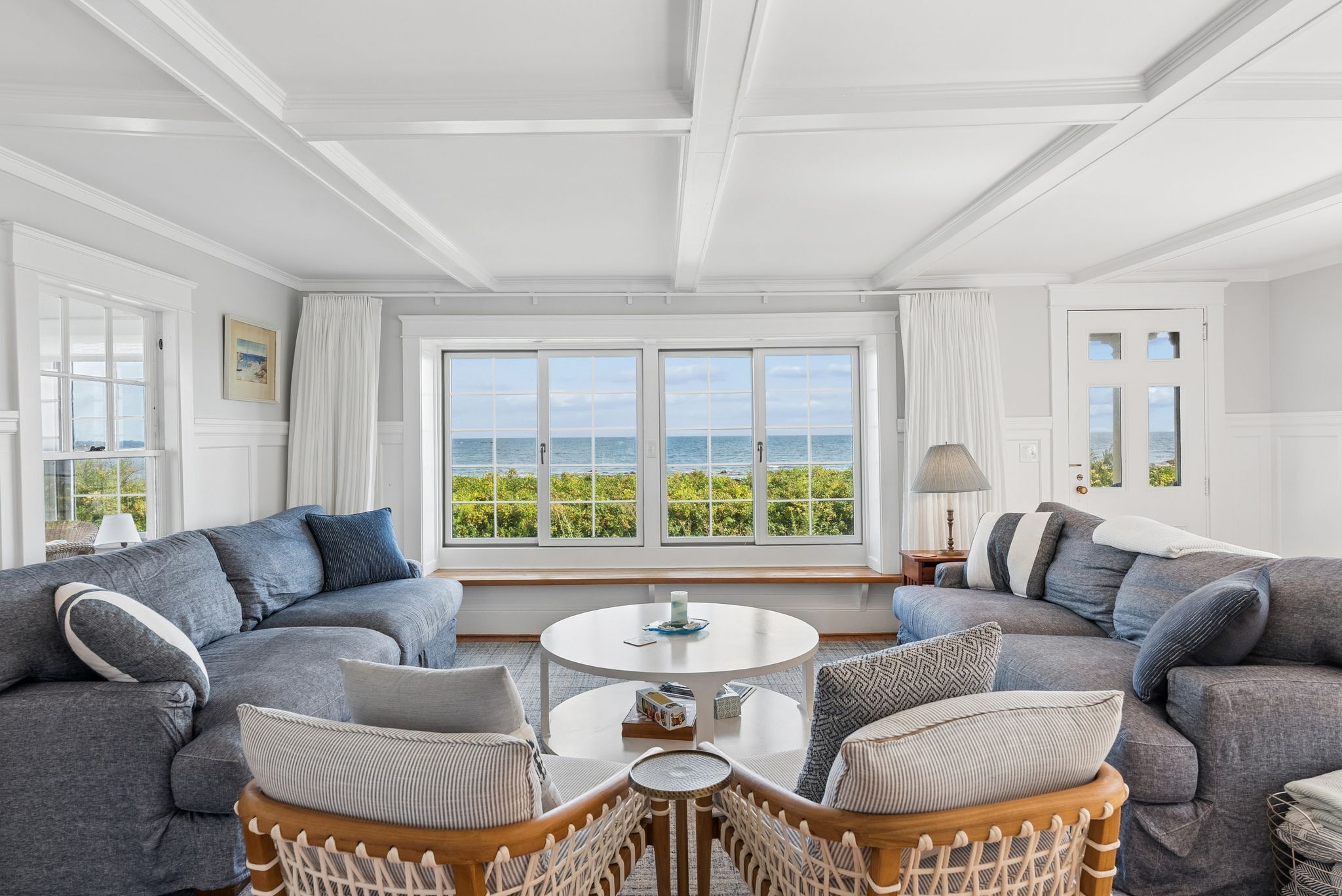 A room with a large window, two sofas, a round coffee table, and a wicker chair.