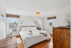 A hotel room with a bed, a desk, a chair, a fan, and a window with a view of buildings. - Ocean Views|HOT TUB|Beach Access| Pet Friendly! (Kennebunk)