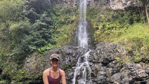 A person sitting on rocks by a waterfall in a natural setting.