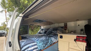 A van converted into a mobile home with a bed, a kitchenette, and a small bathroom.