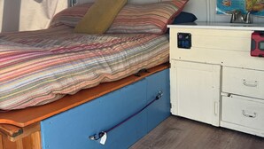 Un intérieur de camping-car compact comprenant un lit, une petite kitchenette et une carte accrochée au mur.