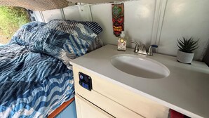 Une petite salle de bain de voyage comprenant un lavabo, une petite plante en pot et un masque décoratif accroché au mur.