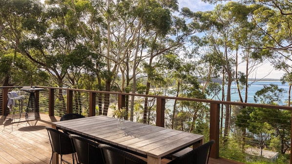 Enjoy a serene view of the water from this outdoor deck, surrounded by lush greenery and comfortable seating.