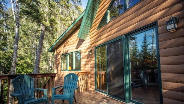 A wooden cabin with large windows and a deck with two chairs. - Timber Bay Lodge & Houseboats (Babbitt)