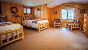 A cozy cabin-style bedroom with a large bed, two smaller beds, a wooden dresser, and a window with a view of the forest. - Timber Bay Lodge & Houseboats (Babbitt)