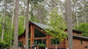 A log cabin with a large deck, surrounded by tall trees. - Timber Bay Lodge & Houseboats (Babbitt)