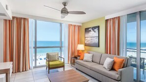 Una camera d'albergo con divano, poltrona e vista sulla spiaggia.