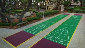 Un terrain de jeu de shuffleboard vert, avec un kiosque et des tables de pique-nique en arrière-plan.