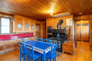 A wooden cabin interior with a dining area, kitchen, and a fireplace. - 915 - Les Immeubles Charlevoix - Domaine Ciel sur Mer (La Malbaie)