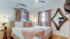 A neatly made bed with a white comforter and a pink throw blanket, a bedside table with a lamp, and a ceiling fan. - Blushing Flamingo- Pool + Putting, Walk to Beach (Indian Rocks Beach)
