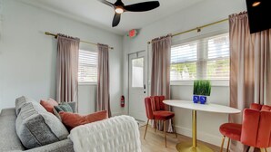 A modern hotel room with a grey sofa, red chairs, a white table, and a ceiling fan. - Blushing Flamingo- Pool + Putting, Walk to Beach (Indian Rocks Beach)