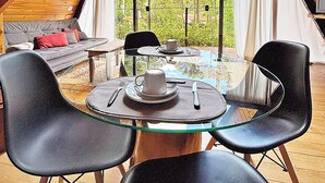 A cozy interior with a glass table, black chairs, a sofa, and a large window offering a view of trees. - Chalet Mon Amour 1 - Pure design in pure air. Hydro, fire pit, pet friendly (Jd do Embaixador Campos do Jordão)