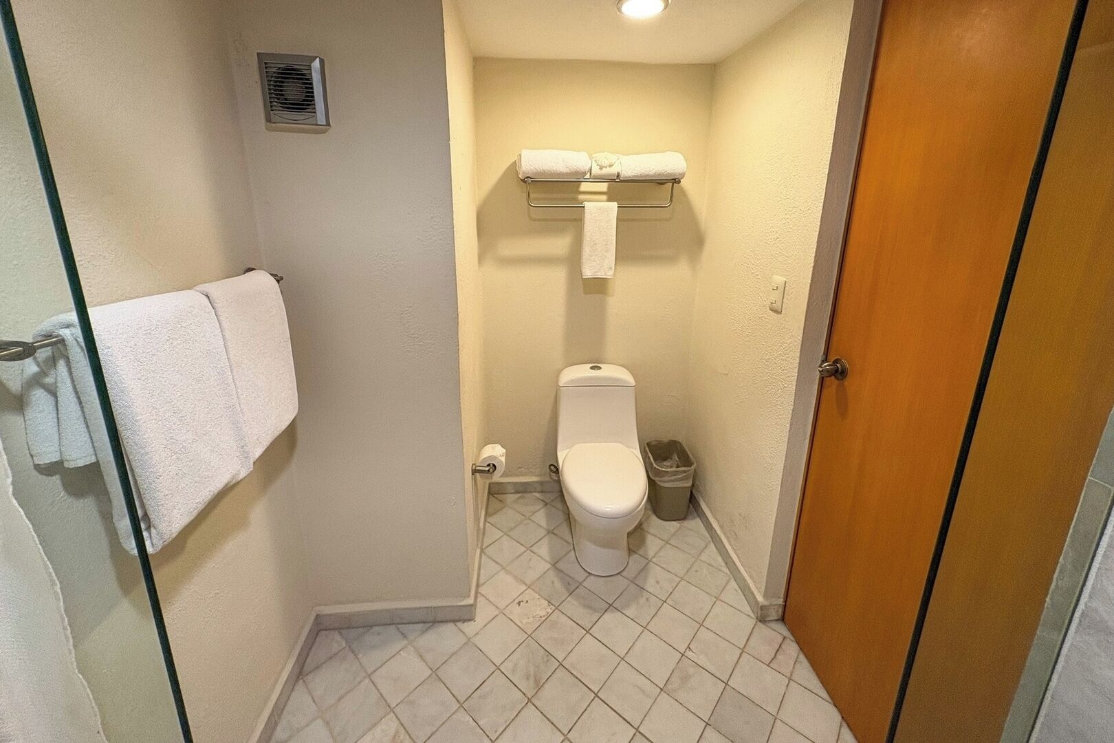 A small, compact bathroom with a toilet, a trash bin, and a towel rack.