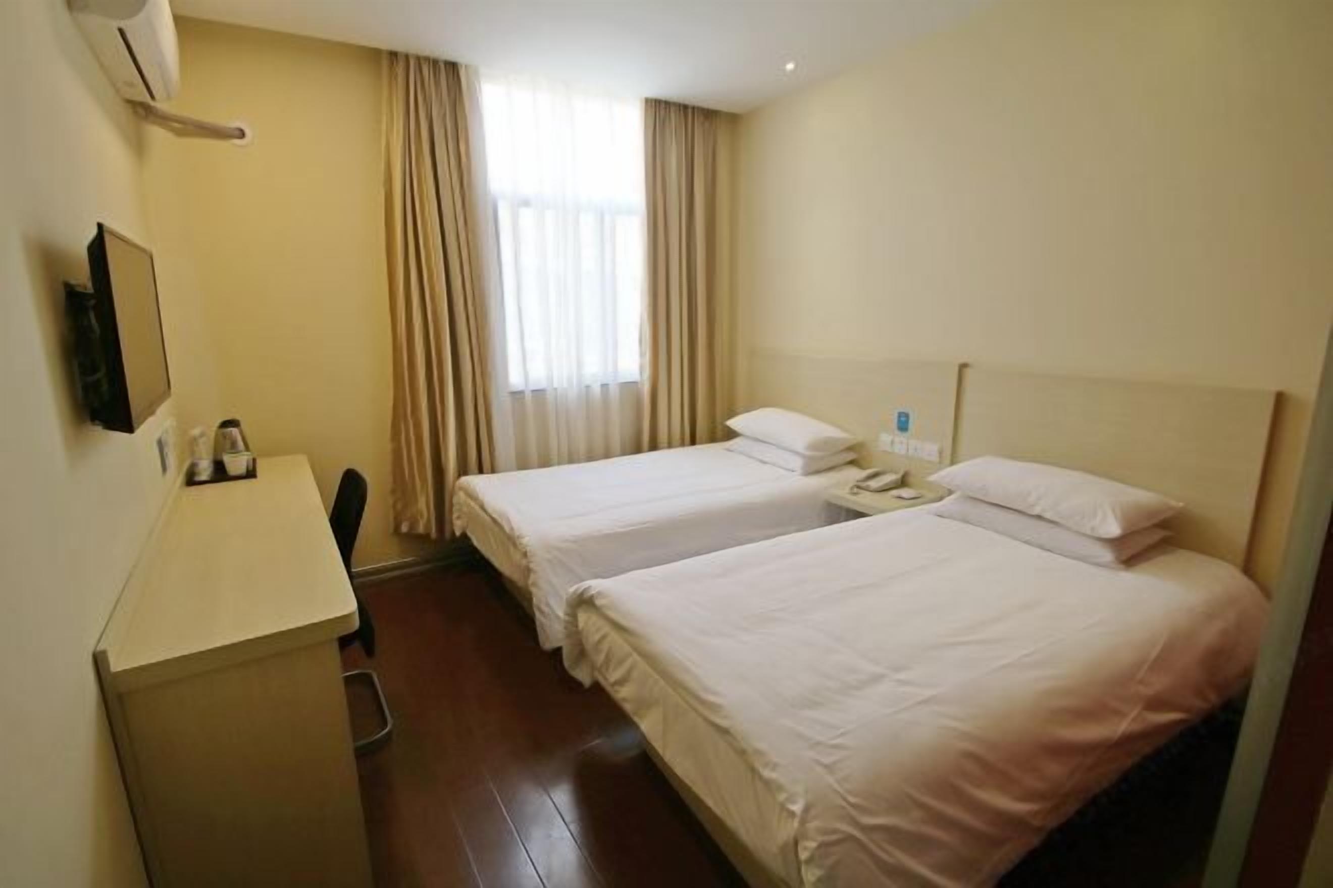 Ein Hotelzimmer mit zwei Betten, einem Schreibtisch, einem Stuhl, einem Telefon und einem Fenster mit Vorhängen.