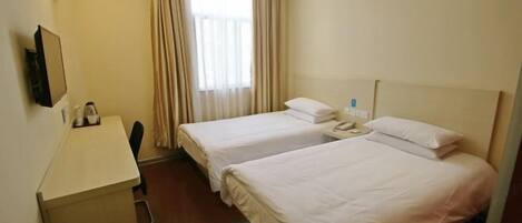 Ein Hotelzimmer mit zwei Betten, einem Schreibtisch, einem Stuhl, einem Telefon und einem Fenster mit Vorhängen.