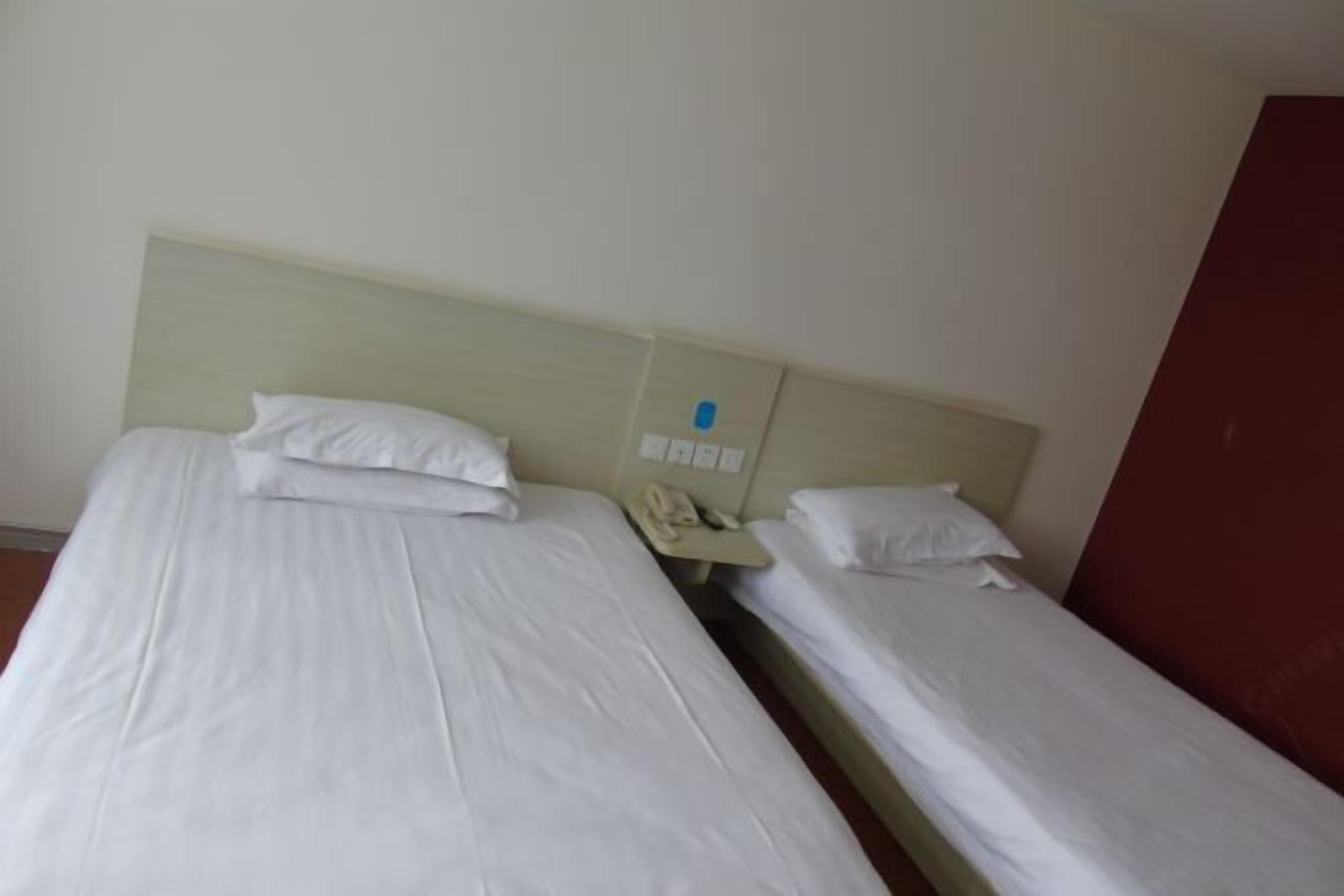 Two single beds with white linens, a bedside telephone, and a red wall.